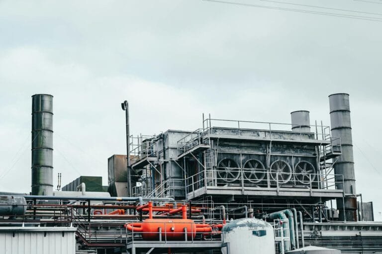 Industrial factory with metal pipes and special equipment surrounded with fences located against cloudy sky on street with power lines in town